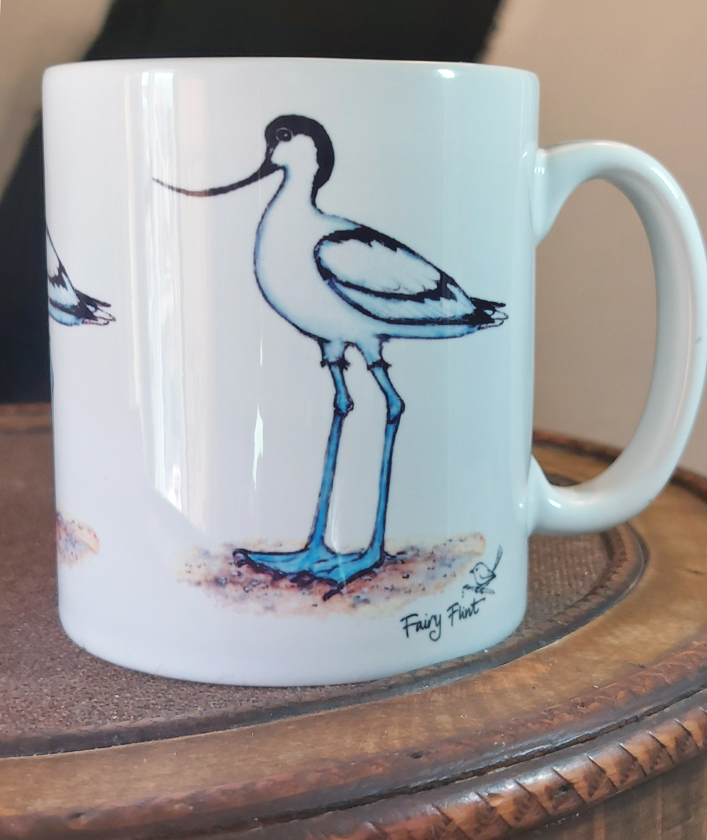 Ceramic mug with Avocet painting eco friendly print by Fairy Flint, mug standing on antique wooden hat box in front of cruck frame interior of 15th century cottage