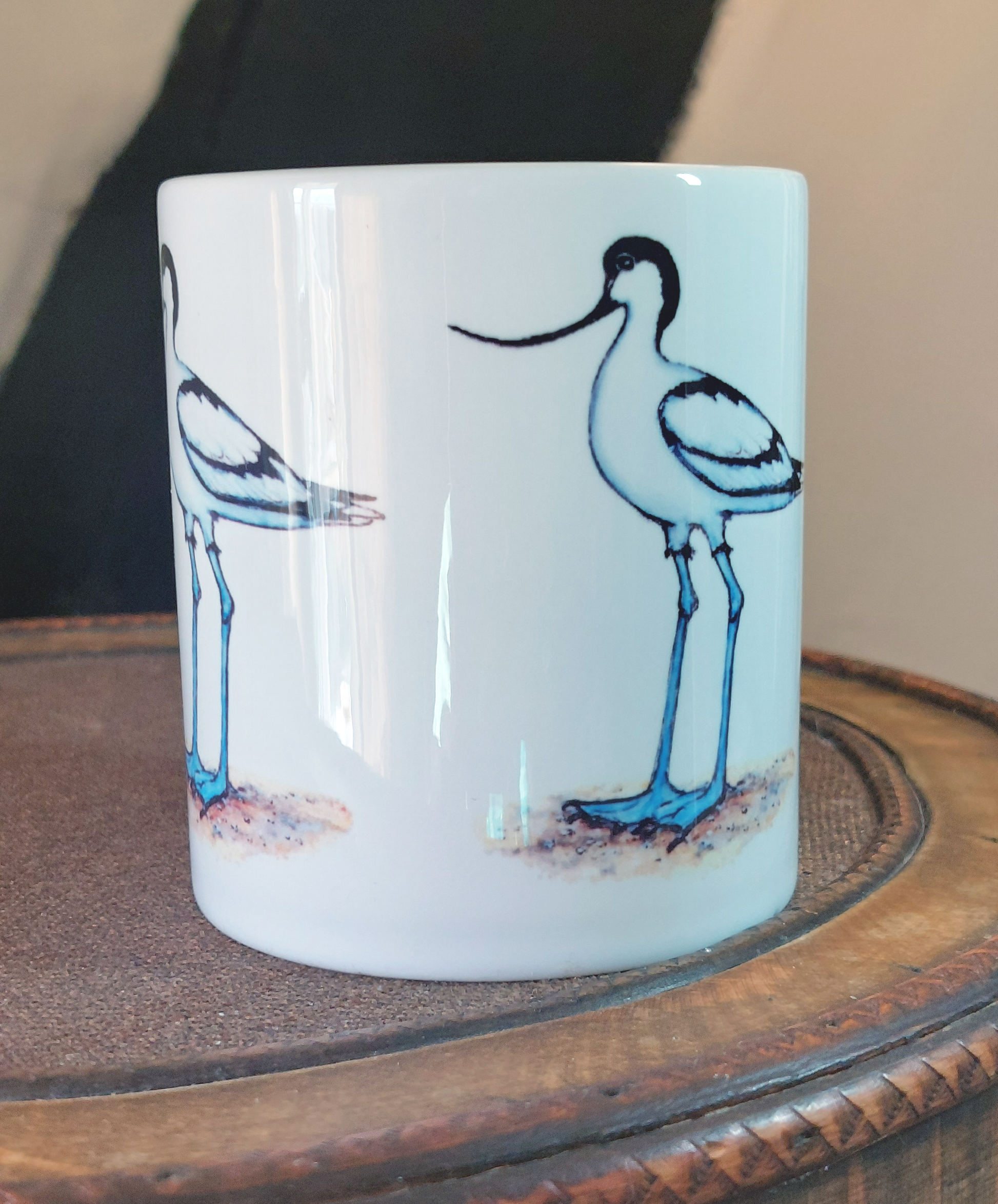 Ceramic mug with Avocet painting eco friendly print by Fairy Flint, mug standing on antique wooden hat box in front of cruck frame interior of 15th century cottage