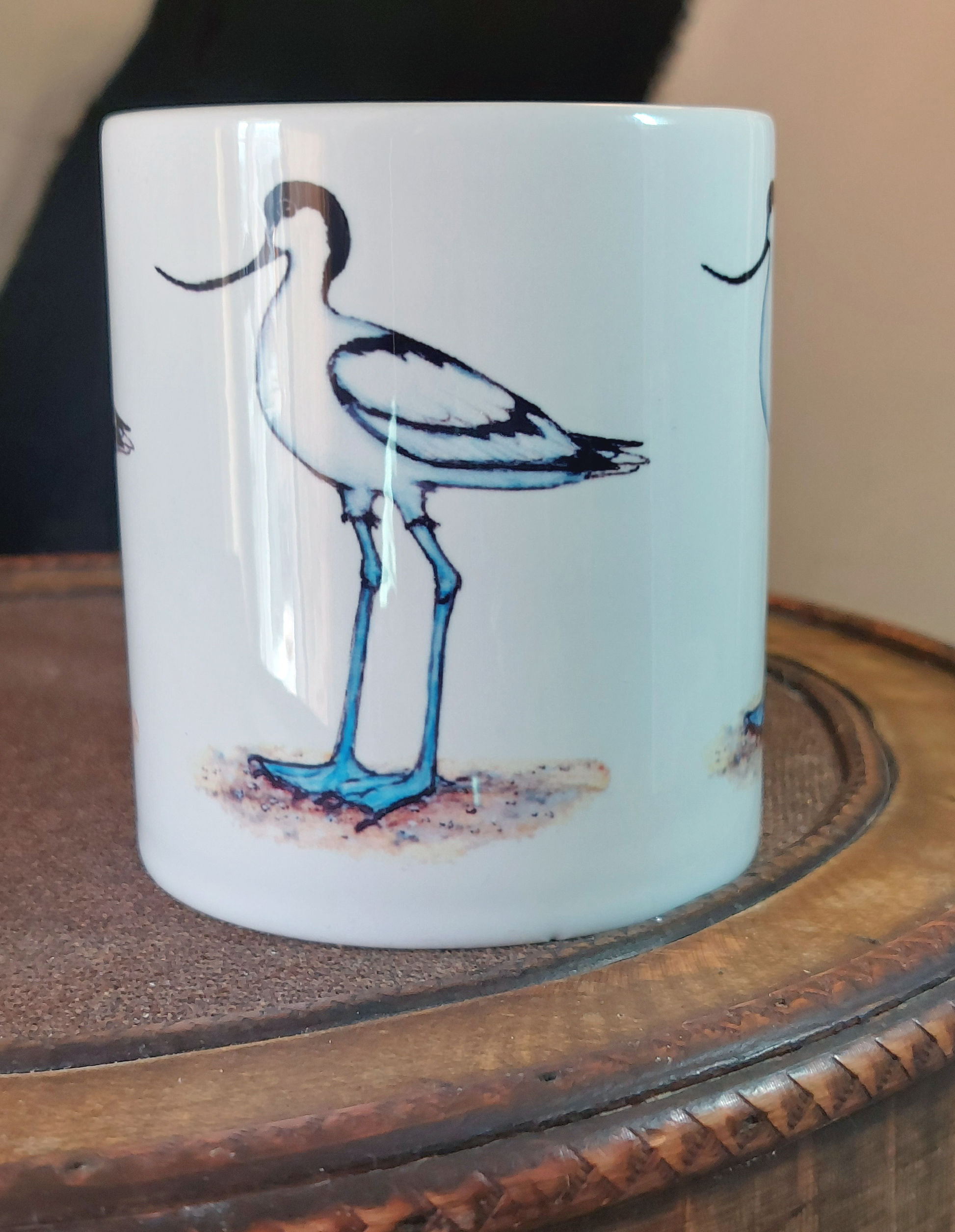 Ceramic mug with Avocet painting eco friendly print by Fairy Flint, mug standing on antique wooden hat box in front of cruck frame interior of 15th century cottage