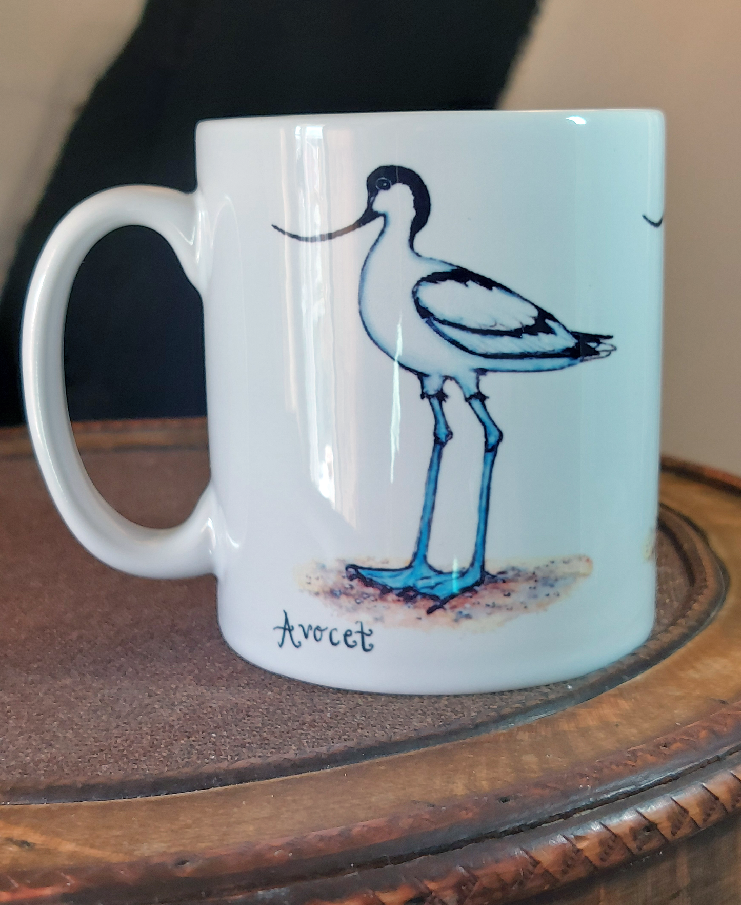 Ceramic mug with Avocet painting eco friendly print by Fairy Flint, mug standing on antique wooden hat box in front of cruck frame interior of 15th century cottage