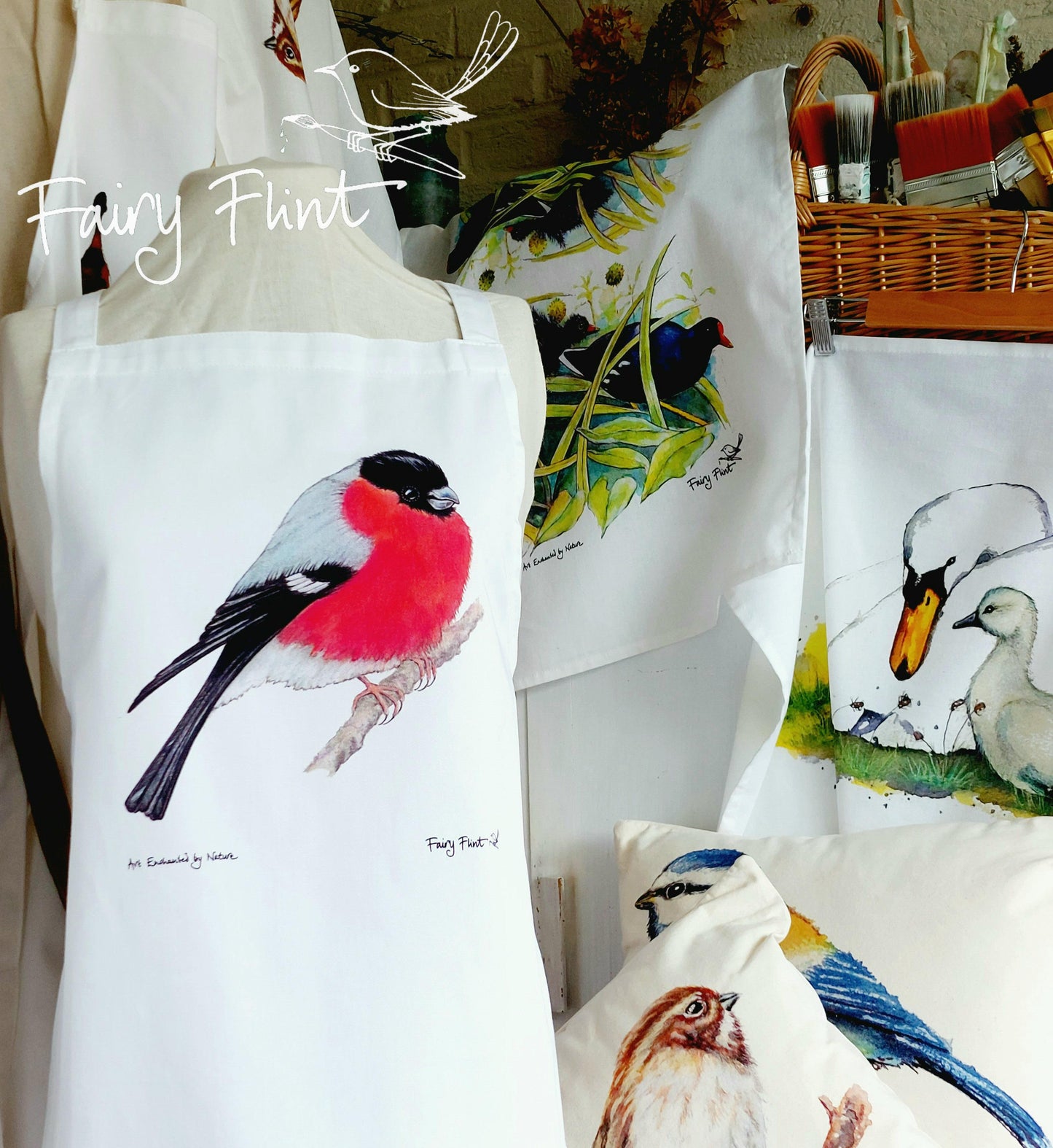 Organic Apron with Bullfinch painting by Fairy Flint printed with eco friendly inks, apron hung on mannequin in front of other aprons with birds, moorhens, ducks and swans on