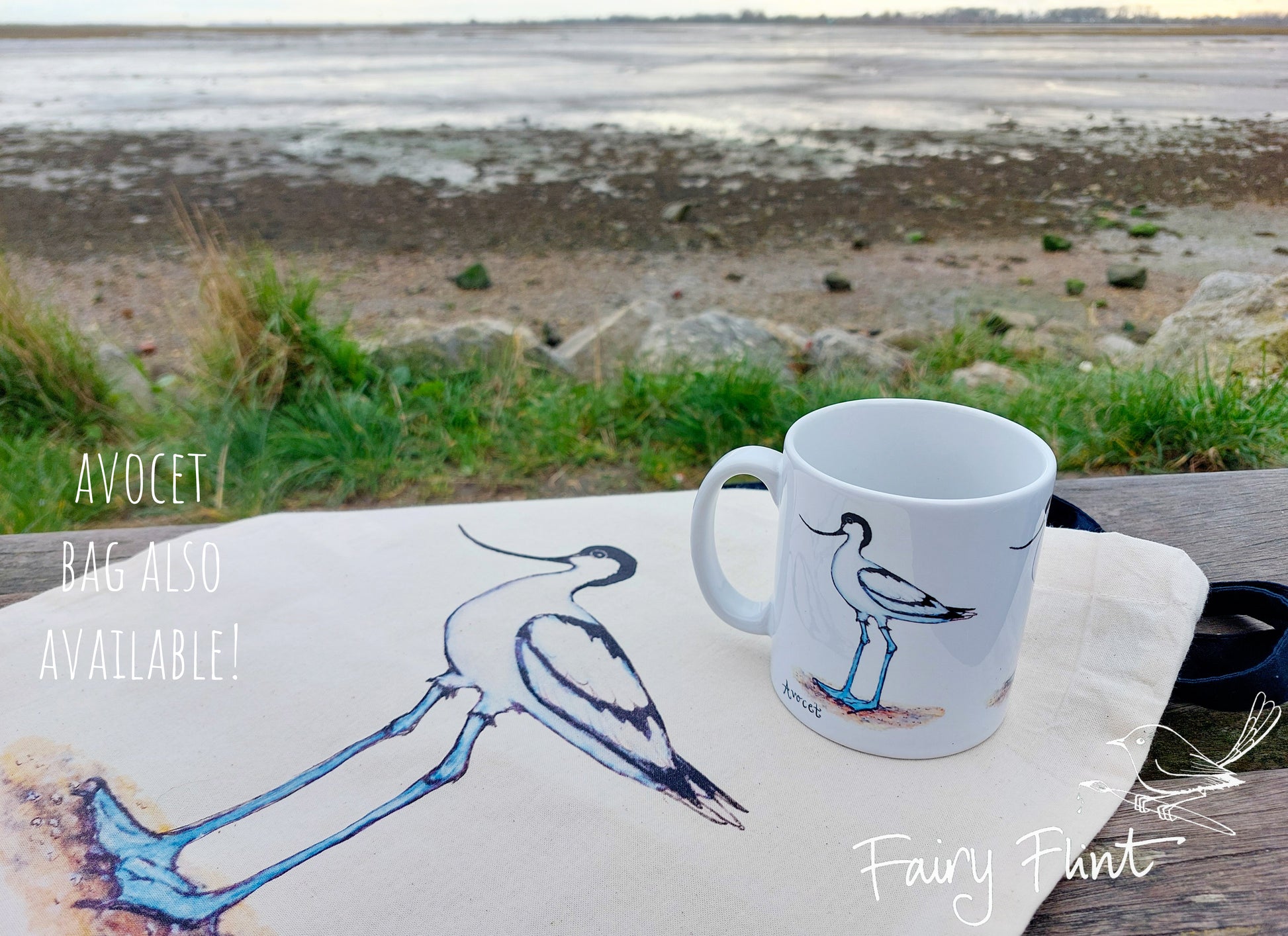 Ceramic mug with Avocet painting eco friendly print by Fairy Flint, photoshoot at Emsworth, mug standing on Canvas Avocet bag, coastline, beach and sea in background