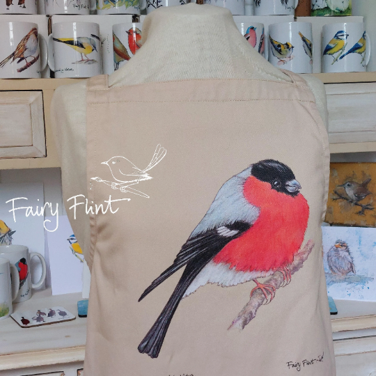 Organic Apron with Bullfinch painting by Fairy Flint printed with eco friendly inks, apron hung on mannequin in front of other aprons with birds, moorhens, ducks and swans on