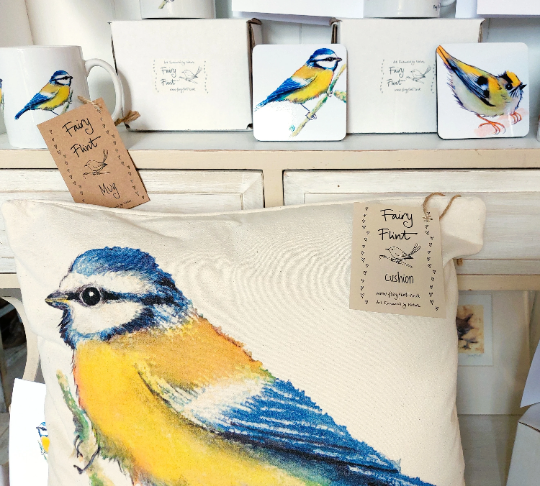 Canvas natural cushion with eco friendly ink print of Blue tit by Fairy Flint, cushion on dresser with other blue tit mugs coaster and goldcrest coaster behind behind