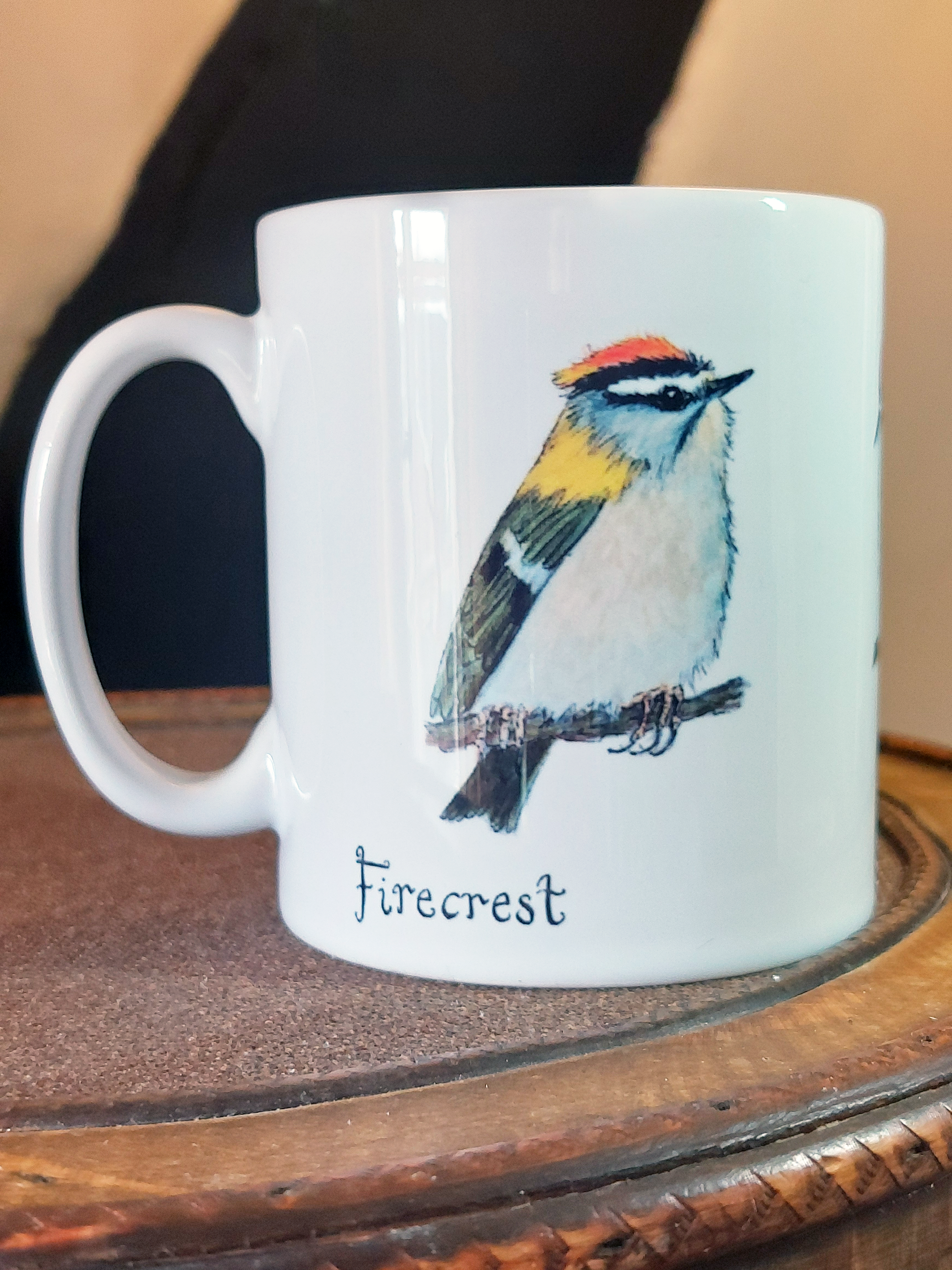 Ceramic mug with Firecrest painting by fairy flint printed with eco friendly inks, mug on amtique wooden hat box in front of cruck frame of 15th century cottage