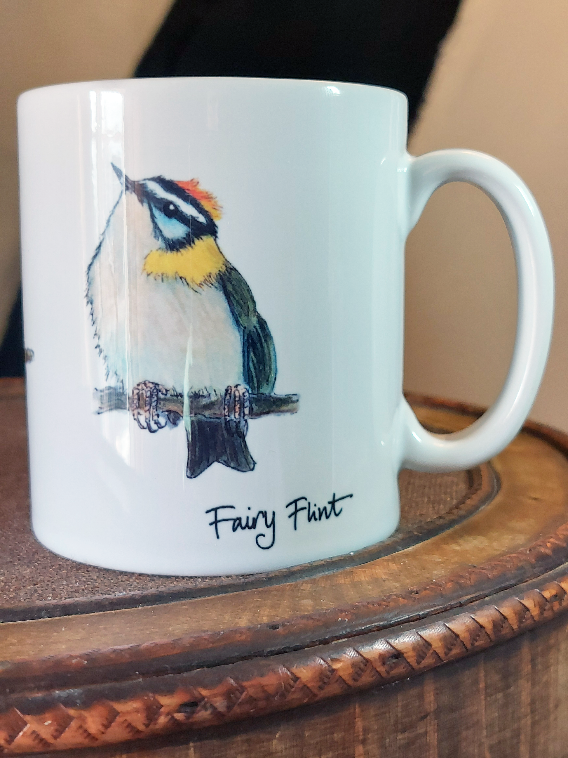 Ceramic mug with Firecrest painting by fairy flint printed with eco friendly inks, mug on amtique wooden hat box in front of cruck frame of 15th century cottage