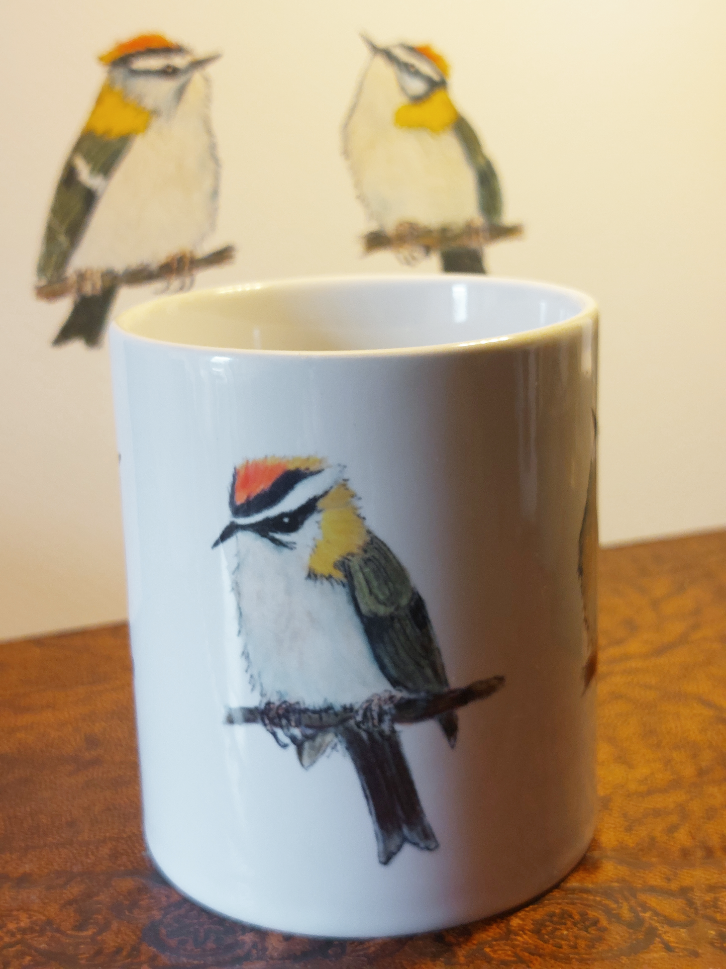 Ceramic mug with Firecrest painting by fairy flint printed with eco friendly inks, mug on amtique wooden hat box in front of cruck frame of 15th century cottage