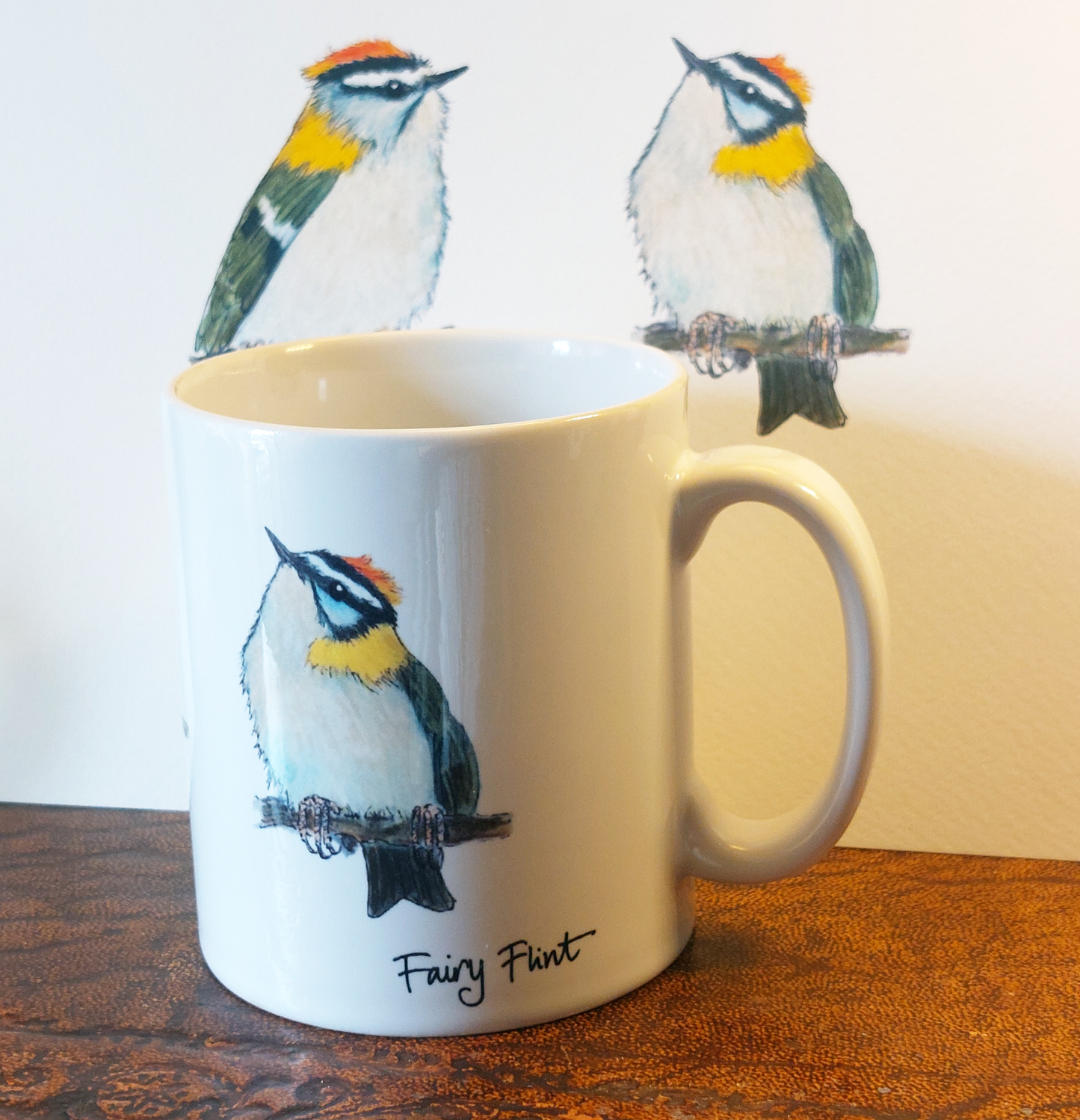 Ceramic mug with Firecrest painting by fairy flint printed with eco friendly inks, mug on amtique wooden shelf in front of print of Firecrests